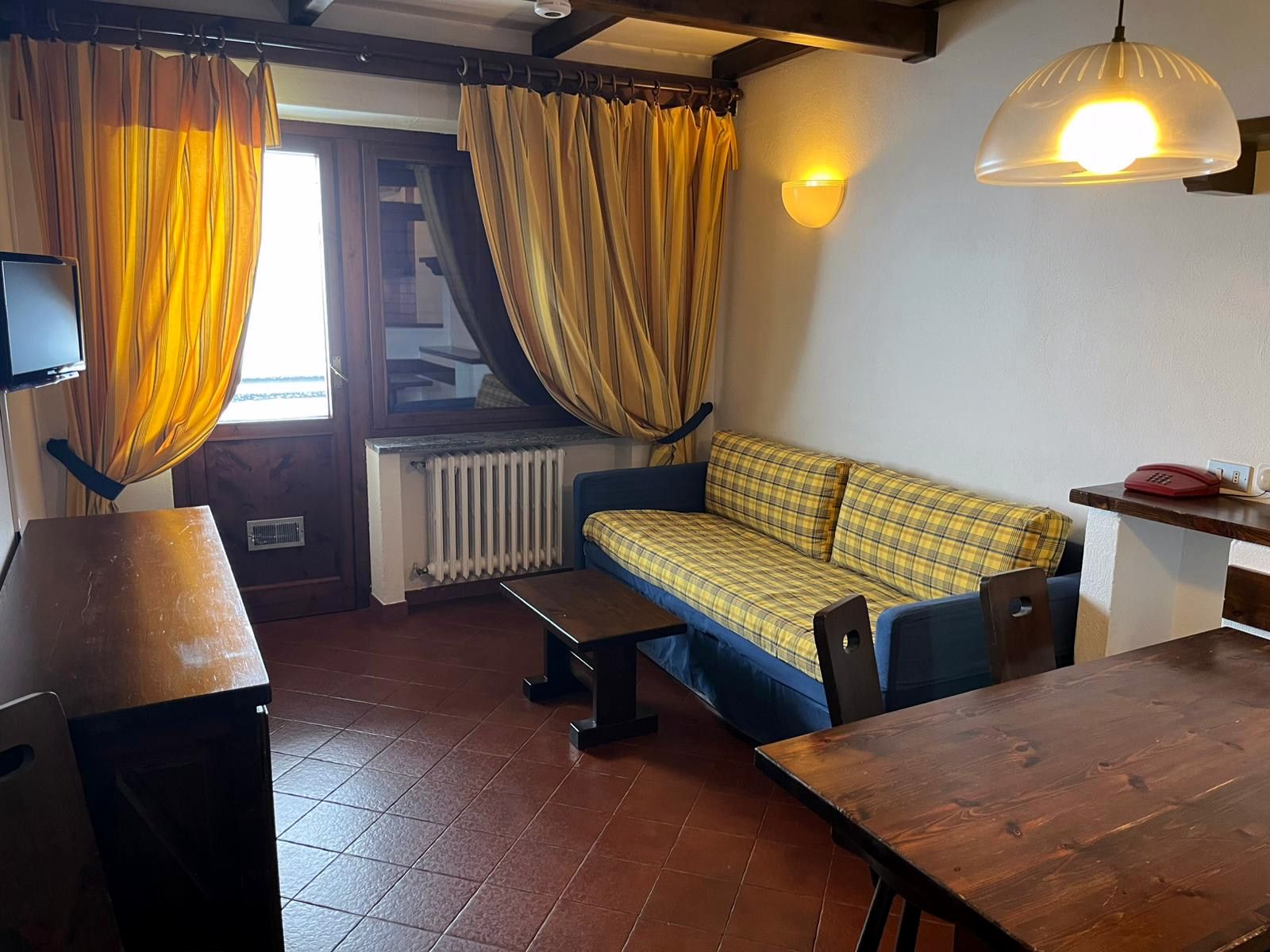 Soggiorno con divano letto doppio a quadri, tavolo in legno, TV e porta-finestra sul balcone